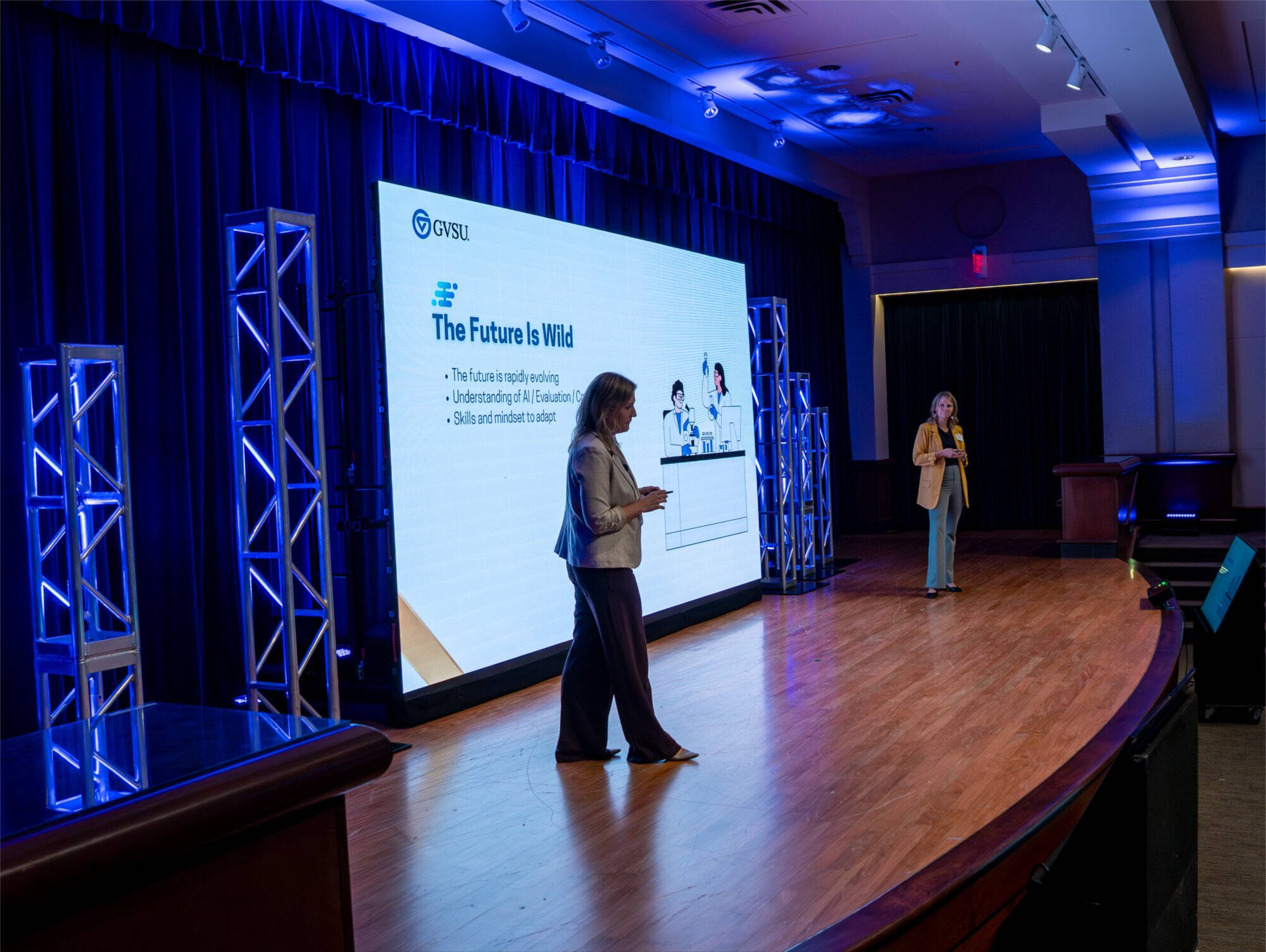 Two presenters stand on stage in front of a large screen displaying a slide titled ‘The Future is Wild’ during a conference session in an auditorium
